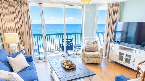 Un salon comprenant un canapé, un fauteuil et un téléviseur, donnant sur un balcon avec vue sur la mer.