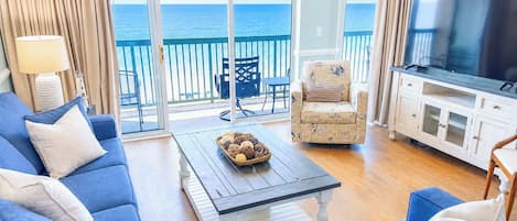 A room with a sofa, a coffee table, a TV, and a view of the ocean.