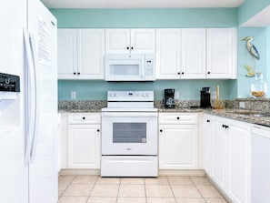 A kitchen with white cabinets, a microwave, an oven, and a coffee maker.