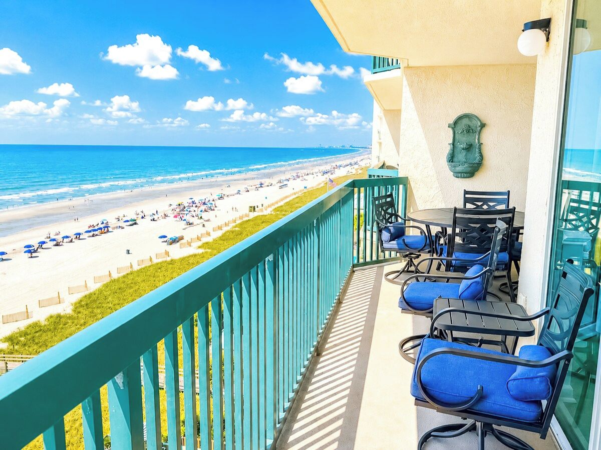 Ein Balkon mit Blick auf einen Strand, Gartenmöbel und einem dekorativen Wandelement.