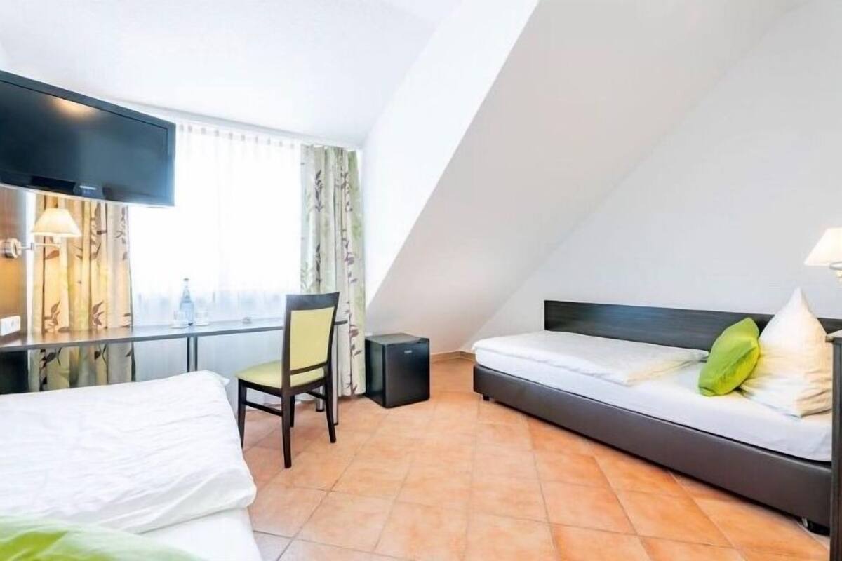 A hotel room with a bed, a desk, a chair, a TV, and a window with curtains.