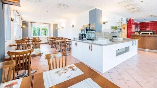 A spacious dining area with wooden tables and chairs, a central island with kitchen appliances, and a bright, well-lit interior.