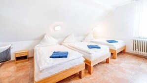 A room with three beds, a small wooden nightstand, a white radiator, and a bathroom with a bathtub.