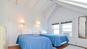 A room with two beds, wooden floors, white walls, and a sloped ceiling.
