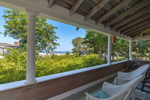 Un espacio de estar al aire libre cubierto, con sillas de mimbre blanco y un banco de madera, con vistas a una playa y vegetación.