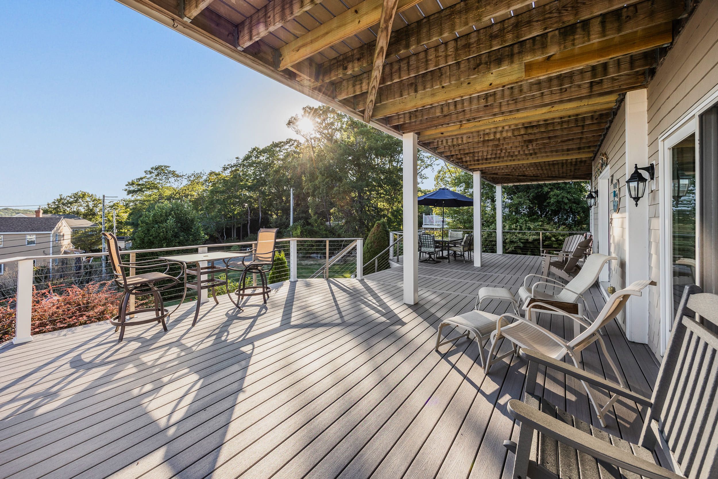A wooden deck with outdoor furniture, including chairs and a table, and a covered area with a railing.