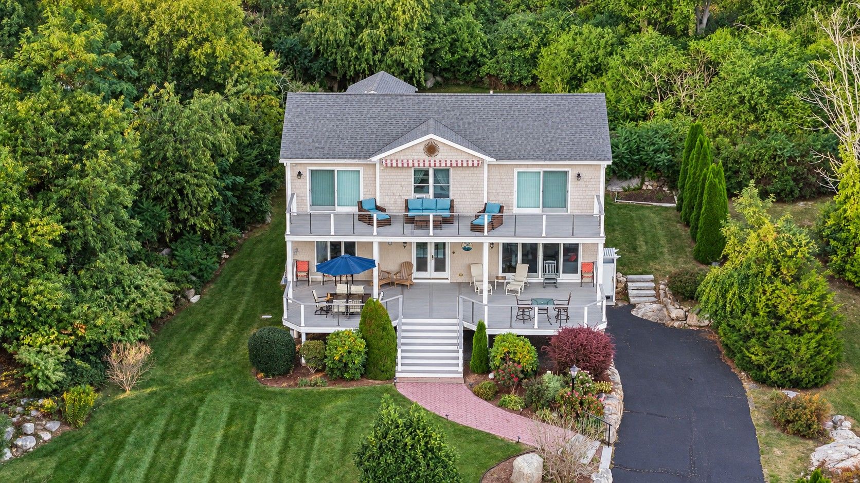 A two-story house with a deck, surrounded by a well-maintained lawn and various shrubs.