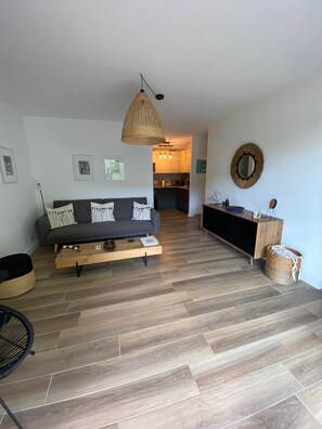A modern living room with a sofa, a dining area, and a kitchen in the background.
