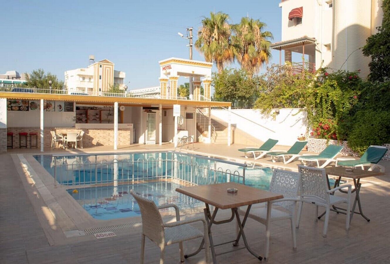 Zona de piscina de un hotel, con piscina transparente, sillas de descanso y una mesa.