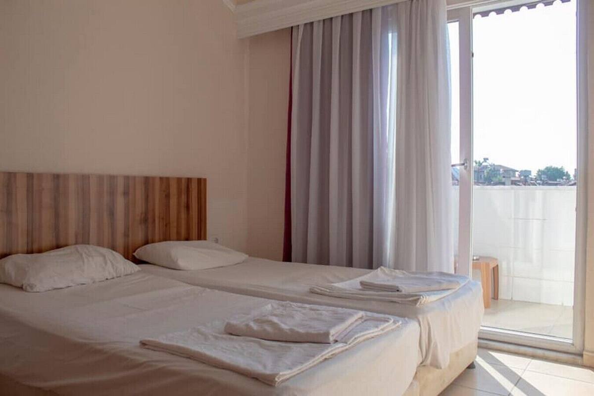 Quarto de hotel com duas camas, uma cabeceira de madeira, uma janela grande com cortinas e vista para o exterior.