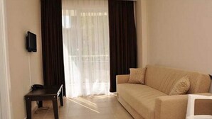 Una sala de estar con un sofá beige, una mesita y un televisor montado en la pared.
