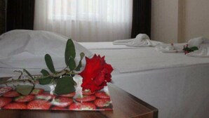 Una habitación de hotel con una cama bien hecha, un jarrón con una rosa roja y una bandeja de fresas.