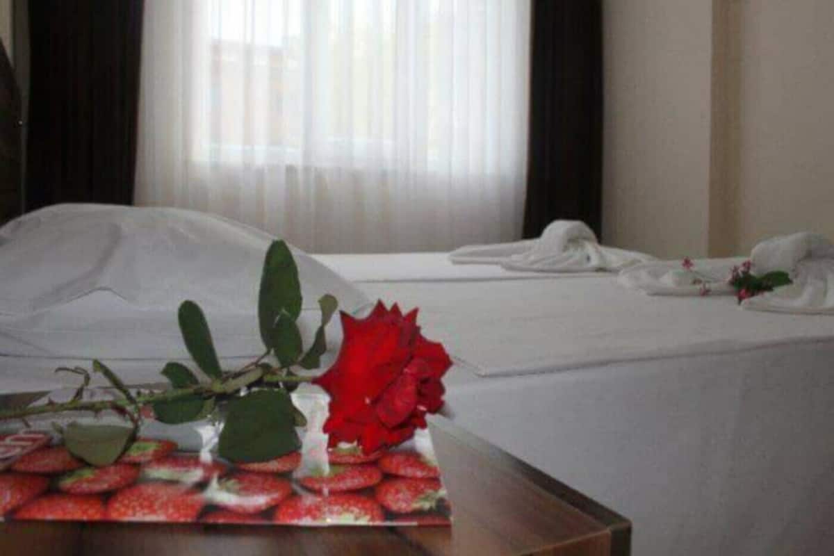 Quarto de hotel com uma cama bem arrumada, um vaso com uma rosa vermelha e uma bandeja de morangos.