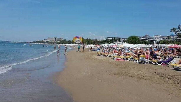 Una playa con arena, sombrillas y gente.