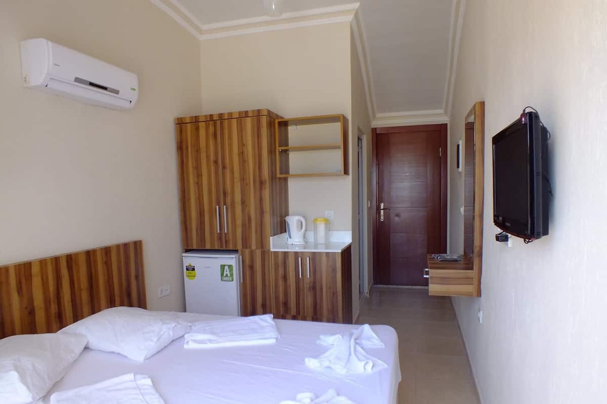 Quarto de hotel com cama, guarda-roupa de madeira, mini-geladeira, pia, espelho e televisão.