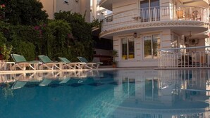 Una piscina cristalina con sillones de descanso y un edificio con balcones.