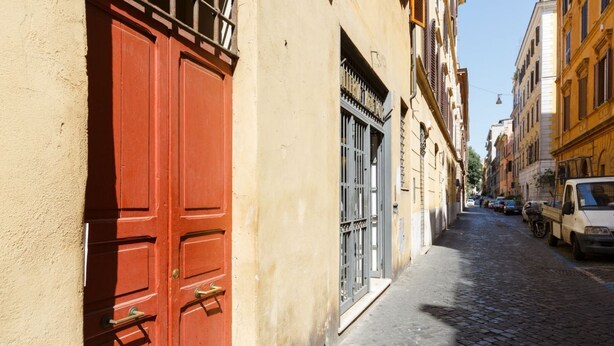 A narrow cobblestone street with buildings on either side, featuring a prominent red door and a metal gate.