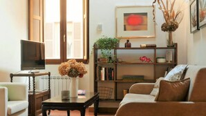 A living room with a television, a bookshelf, a sofa, and a window with shutters.
