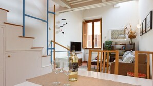 A modern living room with a sofa, a coffee table, and a TV. There is a bottle of wine and two glasses on the table.
