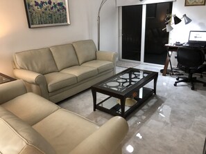 Relax in this stylish living room with a comfortable sofa, desk, and floor lamp, offering a perfect workspace and a view of the outdoors.