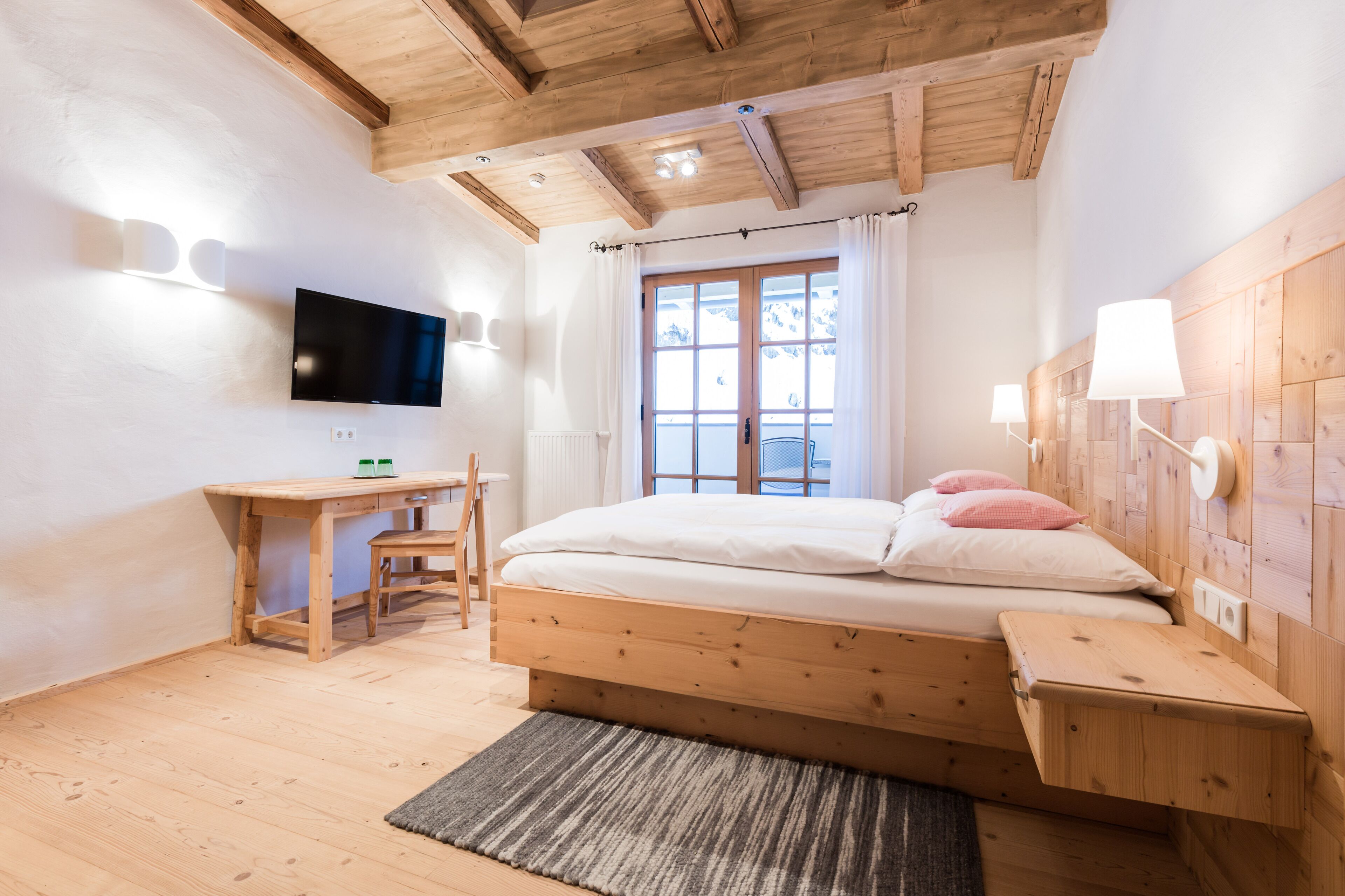 A bedroom with a wooden bed, a desk, a television, and a window with curtains.