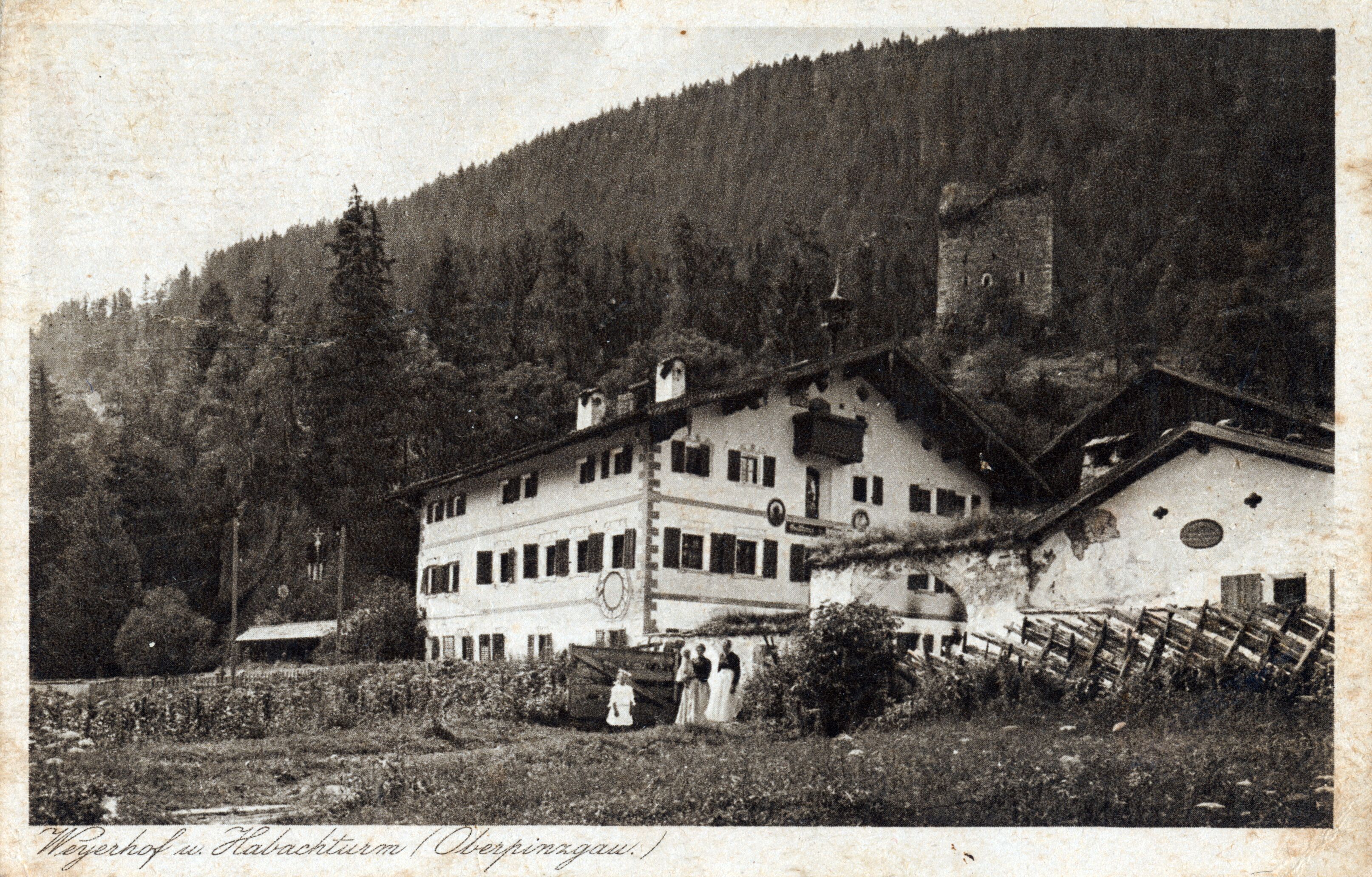 A historical building with a multi-story structure, surrounded by dense forest and a hill.
