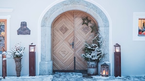 Puerta doble de madera con un diseño de rombos, flanqueada por dos faroles y un pequeño árbol de Navidad.