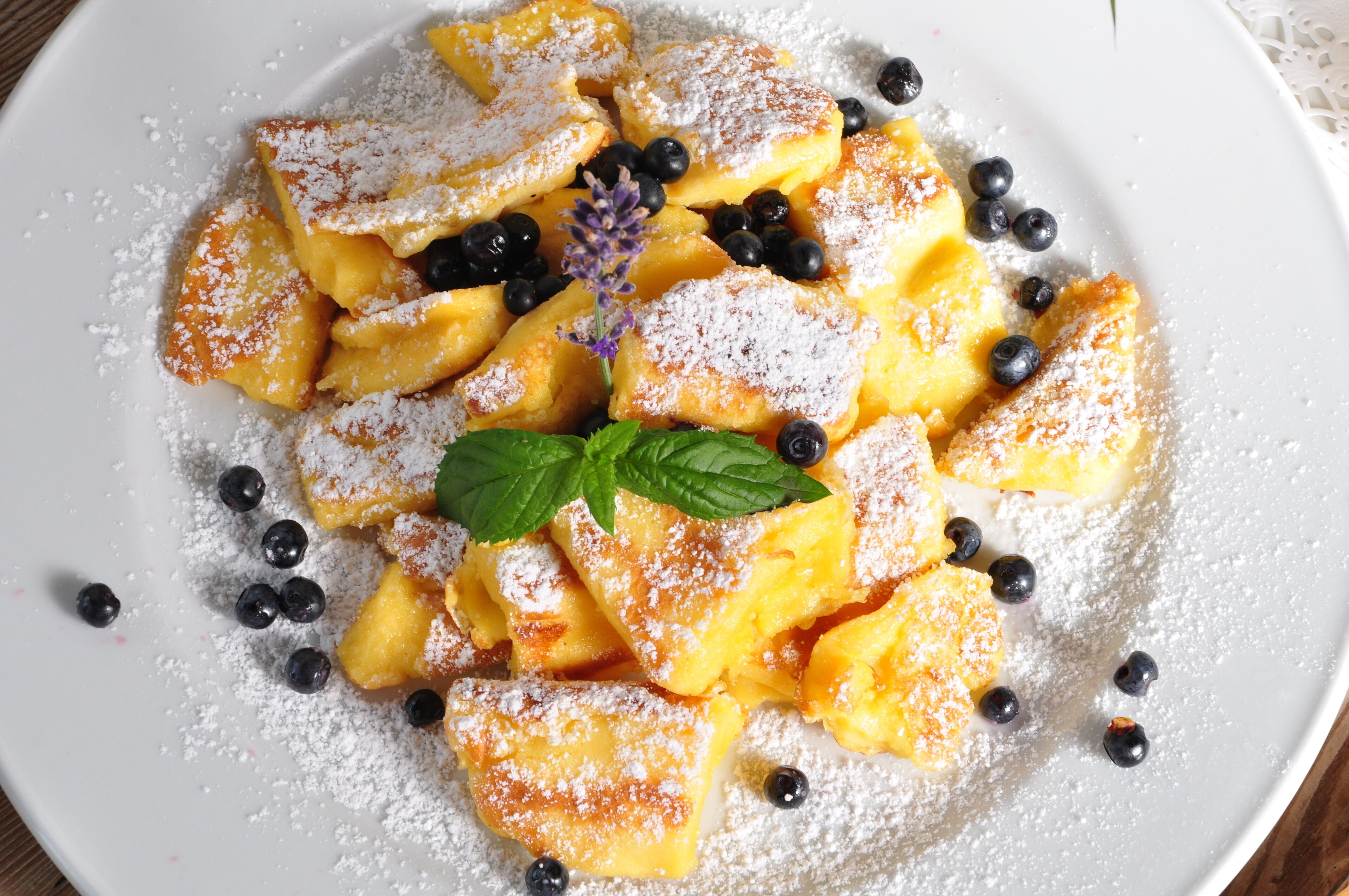 A plate of fruit-filled pastries dusted with powdered sugar and garnished with blueberries and mint.