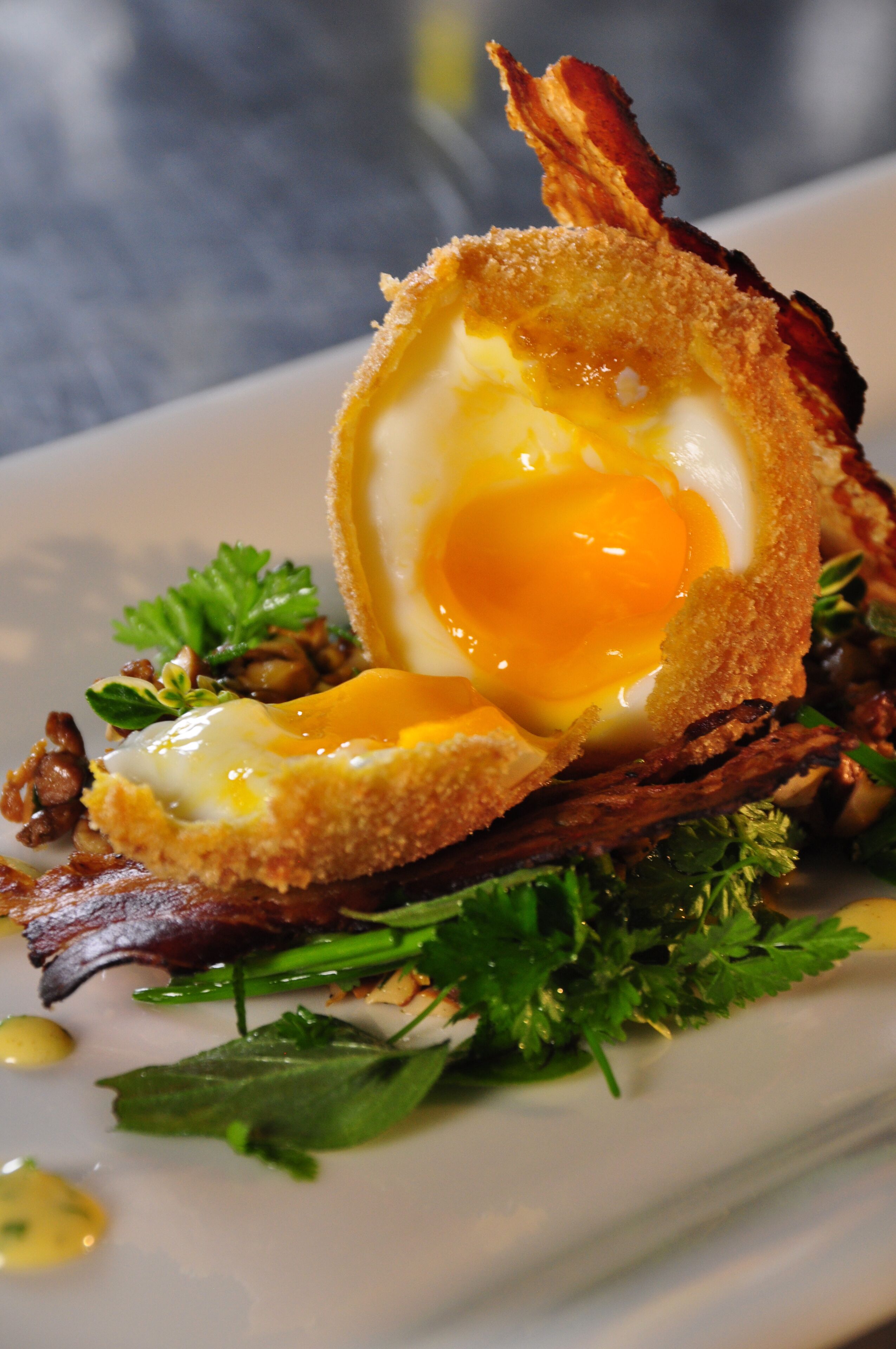 A dish with a fried egg, bacon, and greens on a plate.