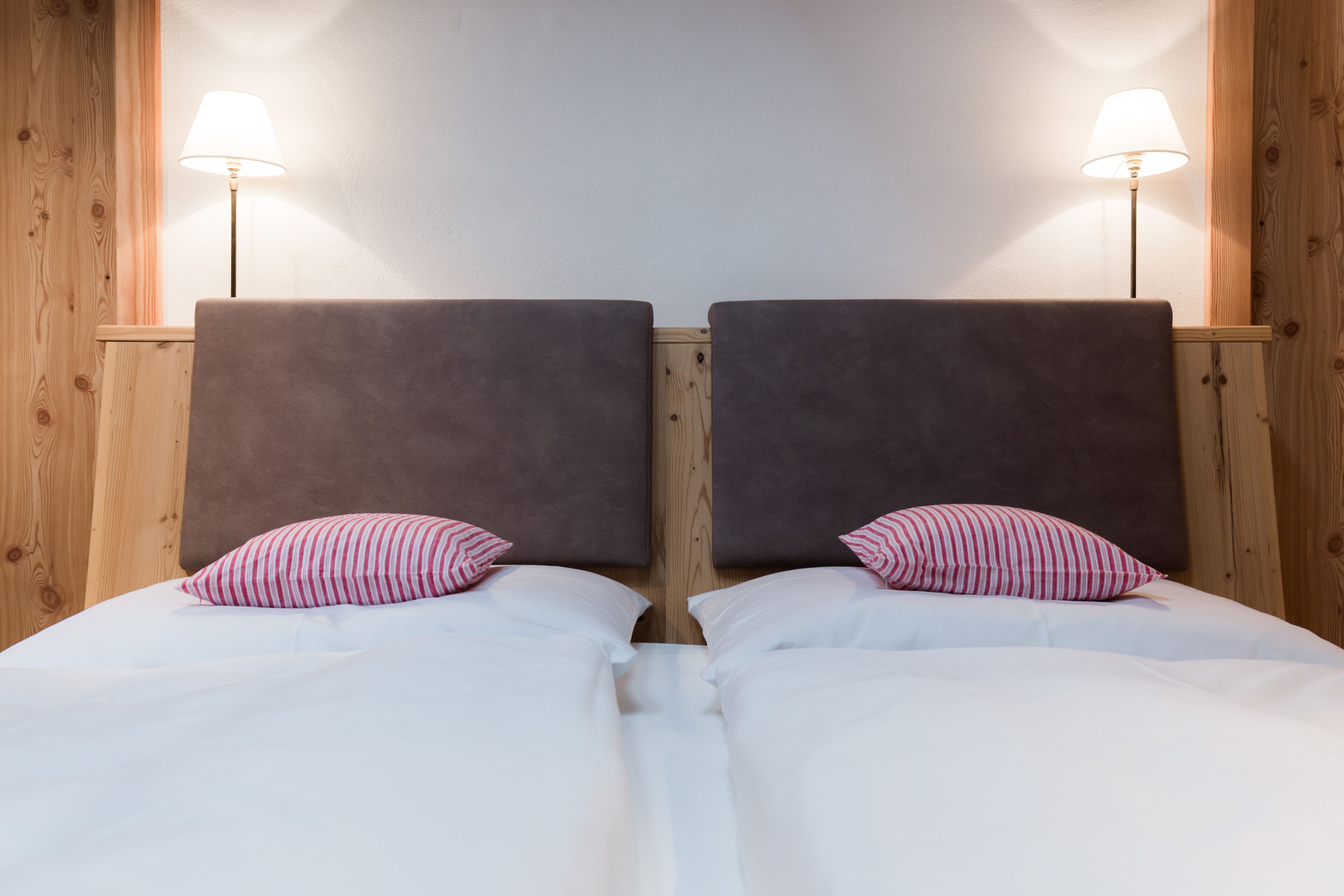 Een tweepersoonsbed met witte beddengoed en twee kussens, omlijst door houten hoofdborden en twee bedlampjes.
