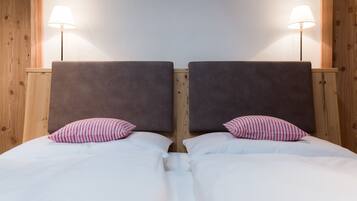 Een tweepersoonsbed met witte beddengoed en twee kussens, omlijst door houten hoofdborden en twee bedlampjes.