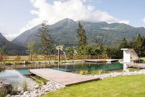 Un paisaje montañoso con una terraza de madera, un estanque pequeño y una construcción de madera.