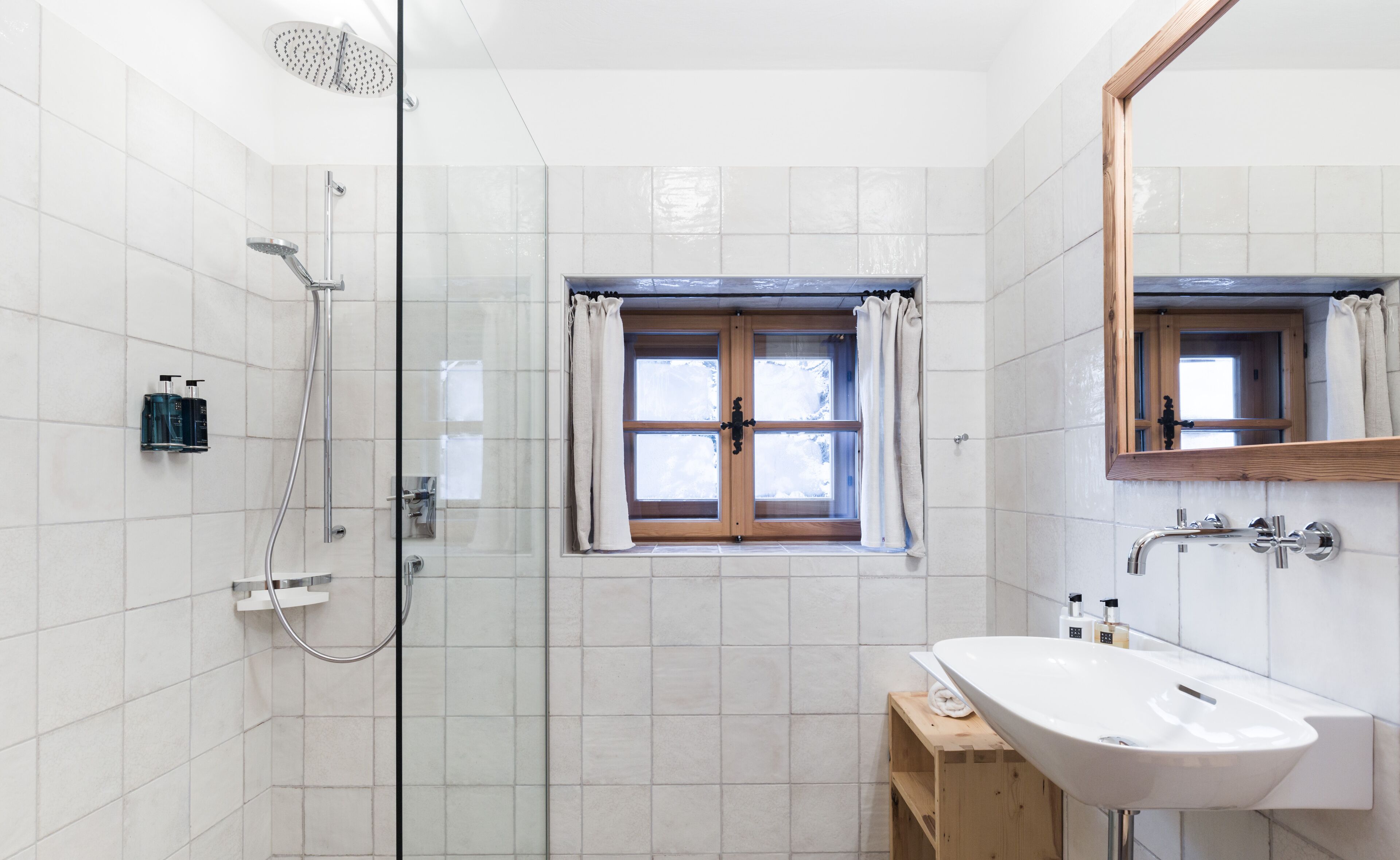 A bathroom with a shower, a window with curtains, a sink, and a mirror.