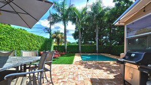 Eine Terrasse mit Backsteinpflaster, Gartenmöbeln, einem Grill und einem Schwimmbecken.