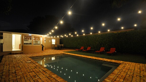 Ein Schwimmbecken mit Ziegelbordurand, einer überdachten Terrasse und einer Lichterkette darüber.