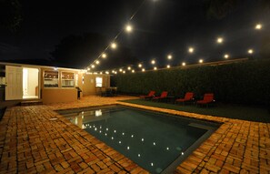 A swimming pool with a brick border, a covered patio area, and a string of lights above. - Heated private pool, walk to Zoo, Science Museum & Park (West Palm Beach)