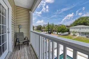 A covered porch with a view of a residential neighborhood, a pool, and a clear sky.