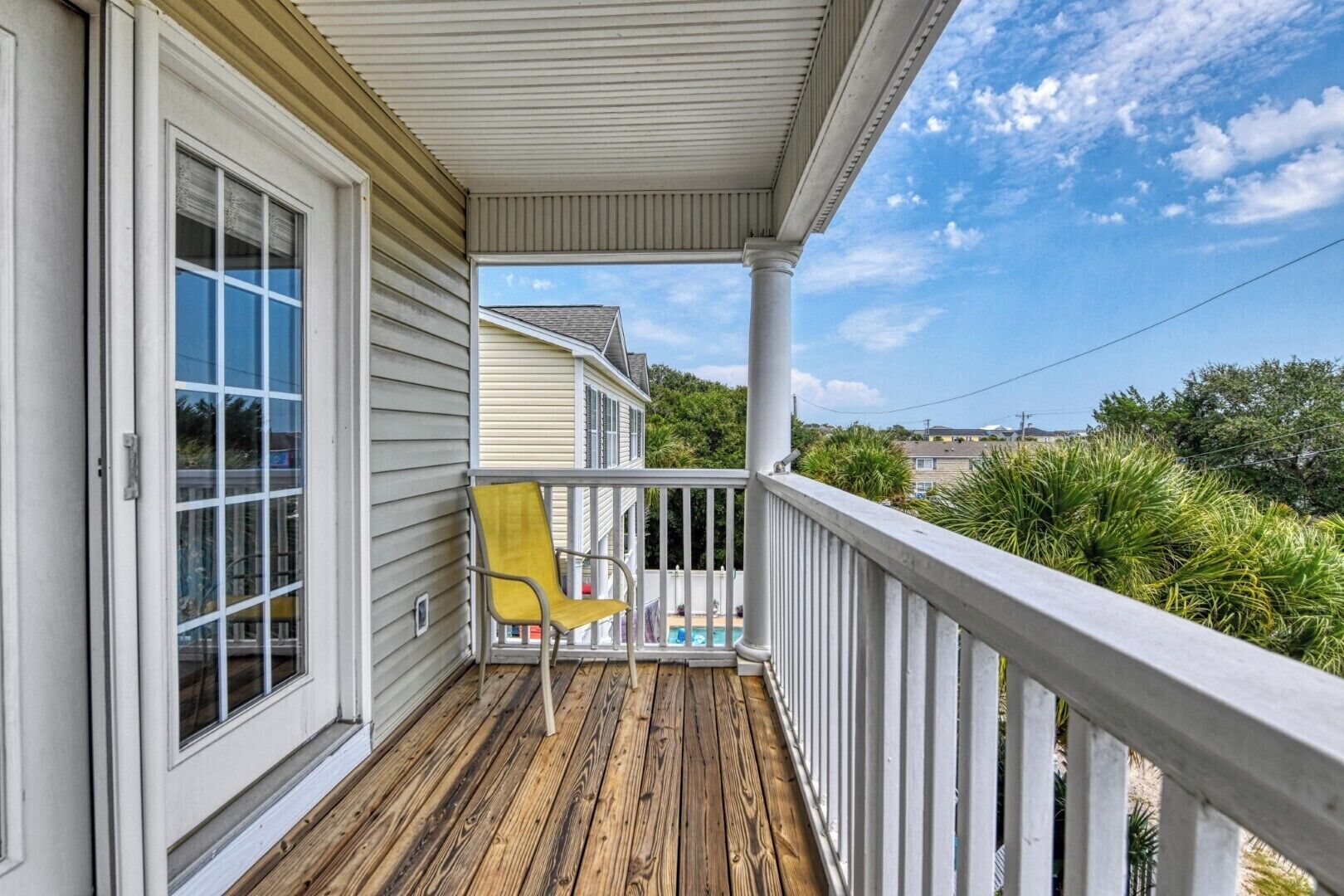 A wooden deck with a yellow chair, a white railing, and a clear view of a residential area.