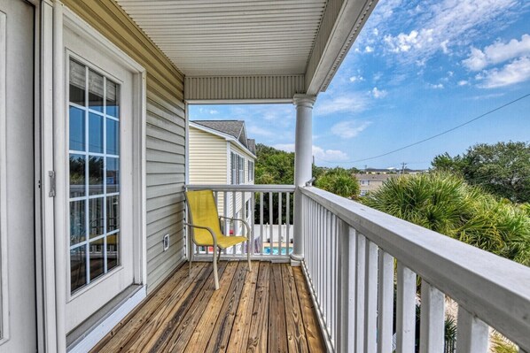 A wooden deck with a yellow chair, a white railing, and a clear view of a residential area.