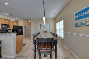 A spacious kitchen with a central island, a dining area with a long table and chairs, and a beach-themed wall decoration.