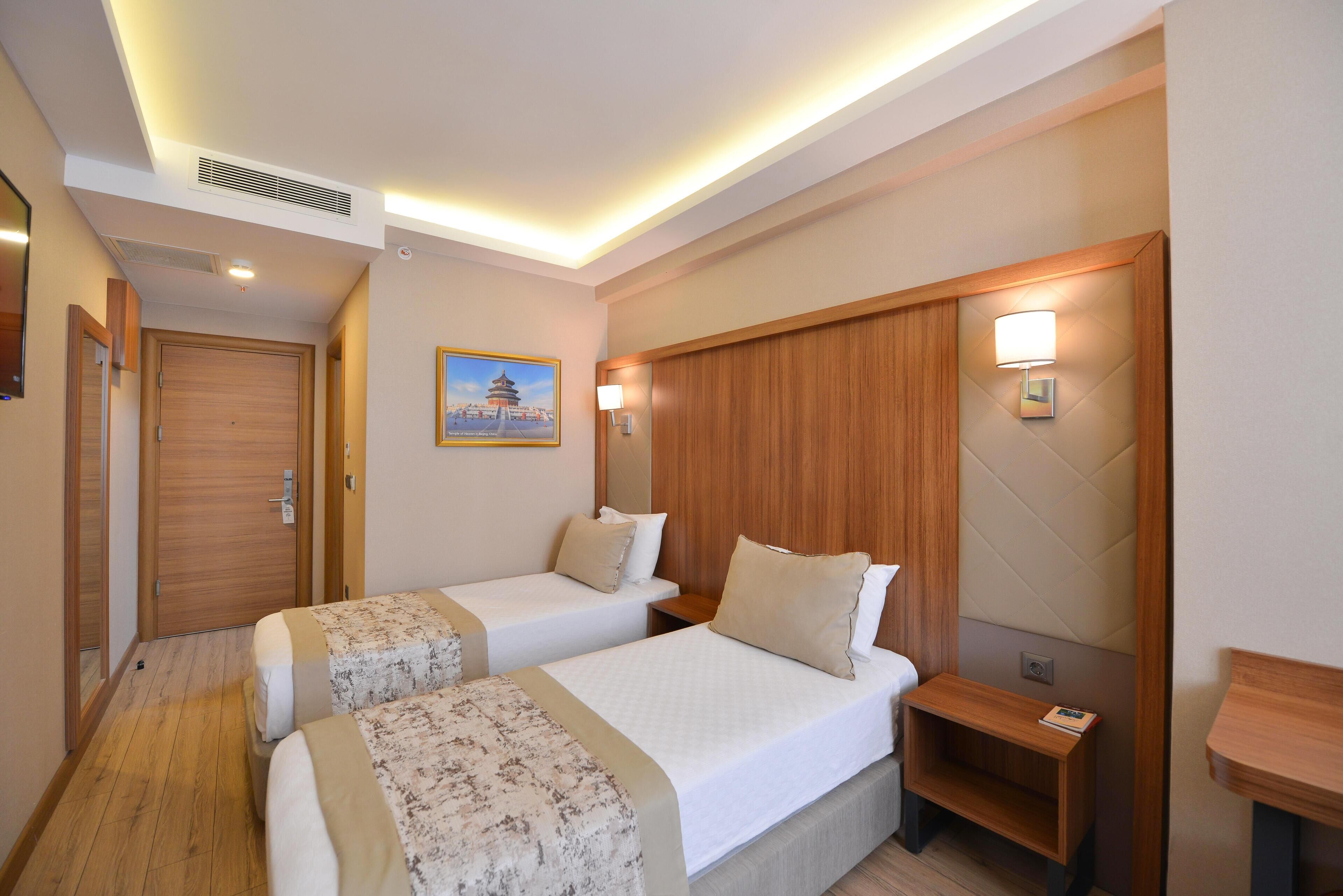Una camera d'albergo con due letti, una testiera in legno, un comodino, una lampada e un quadro appeso al muro.