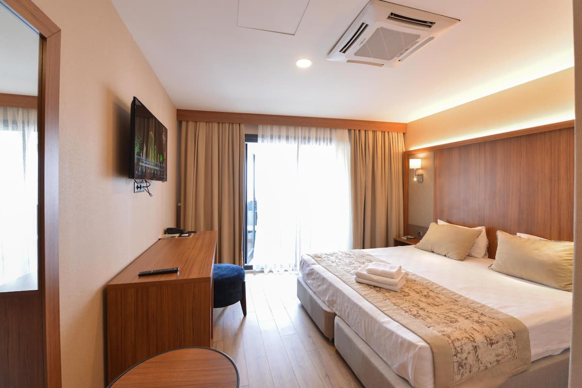 A hotel room with a bed, a desk, a chair, a TV, and a window with curtains.