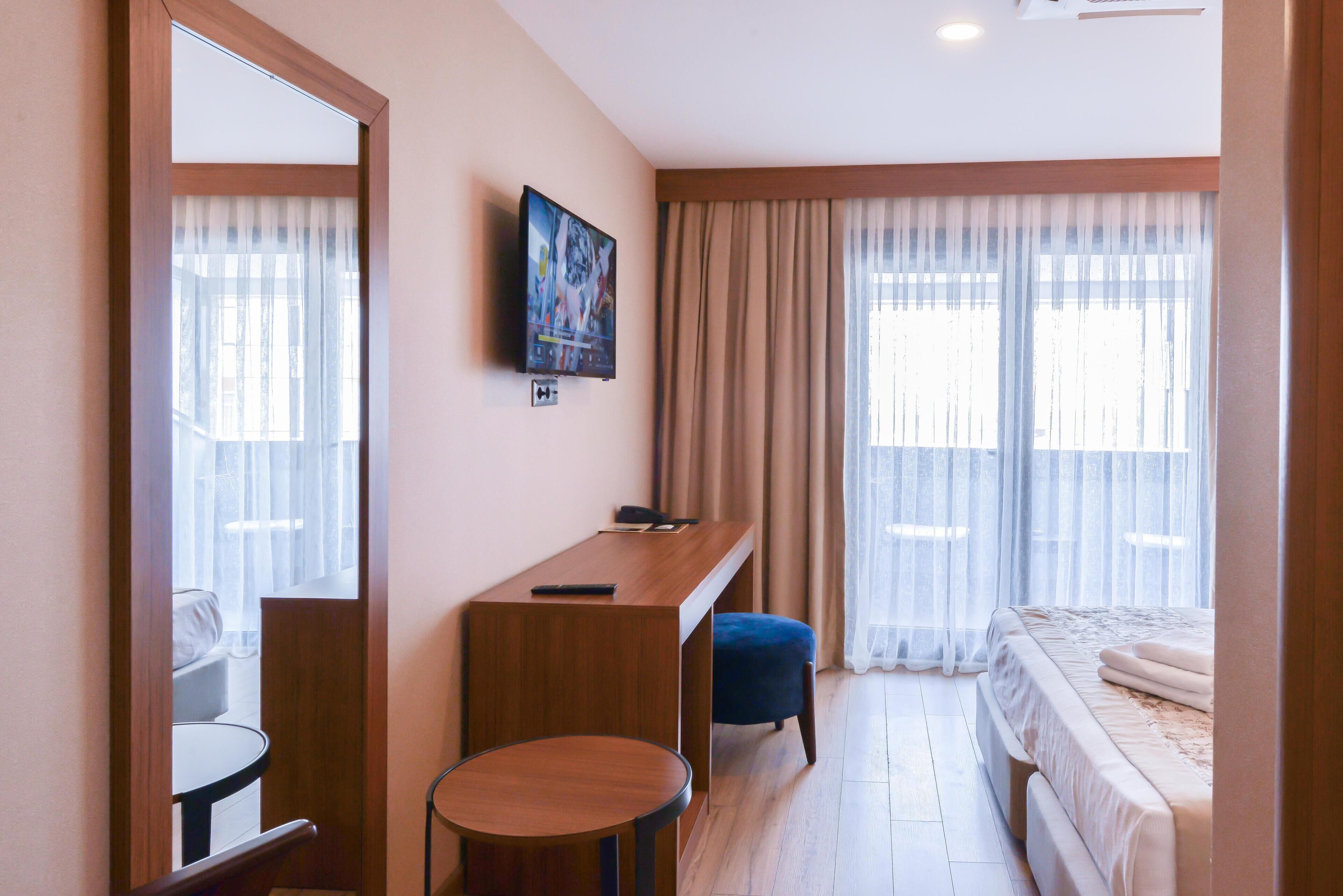 A hotel room with a bed, a desk, a chair, a TV, and a window with curtains.