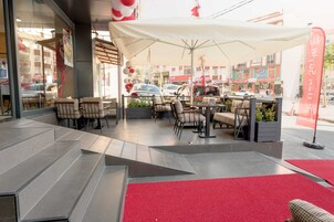 Un espacio exterior con mesas y sillas, alfombra roja y toldo blanco.