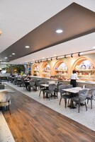Un restaurante moderno con una barra alargada, varias zonas de estar y un cocinero preparando comida.