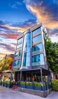 Un hotel moderno con fachada de vidrio, varios pisos y una entrada con alfombra roja.