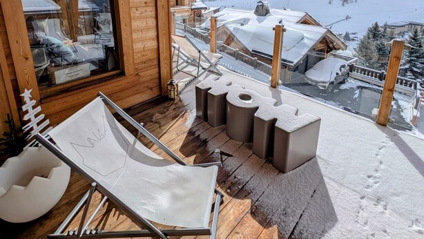 Una baita di legno con un balcone affacciato su un paesaggio montano innevato.
