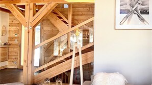 Un ampio loft con travi a vista in legno, un soppalco e una zona salotto accogliente con una calda coperta bianca.
