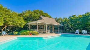 Ein klares, blaues Schwimmbecken mit einem überdachten Pavillon und Liegestühlen.