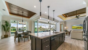 Une cuisine spacieuse dotée d’un grand îlot central, de luminaires suspendus modernes et d’un ventilateur de plafond.